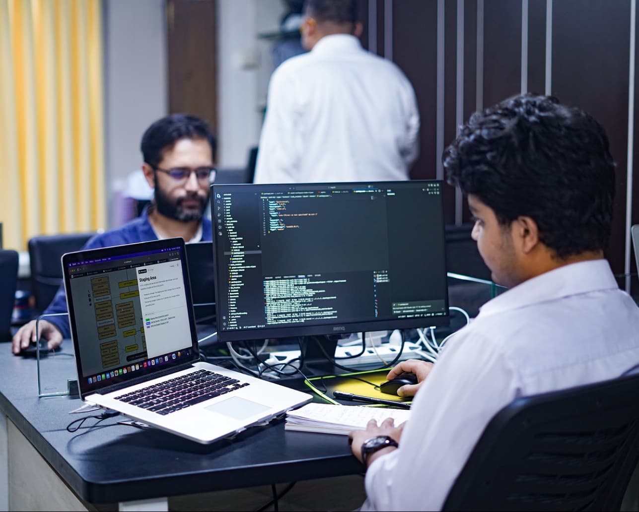 Engineering team collaborating around monitors displaying blockchain code and smart-contract dashboards