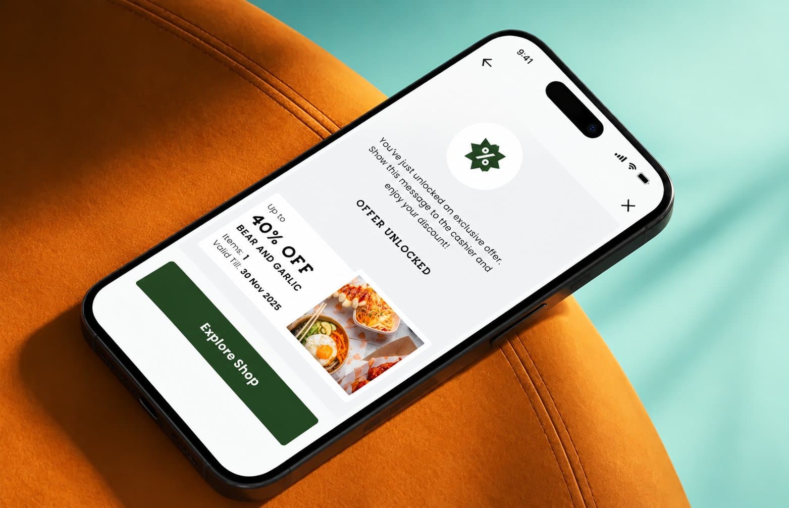 Phone lying on an orange velvet chair showing the Camden Market app Offer Unlocked screen with a 40% off Bear and Garlic deal and an Explore Shop button
