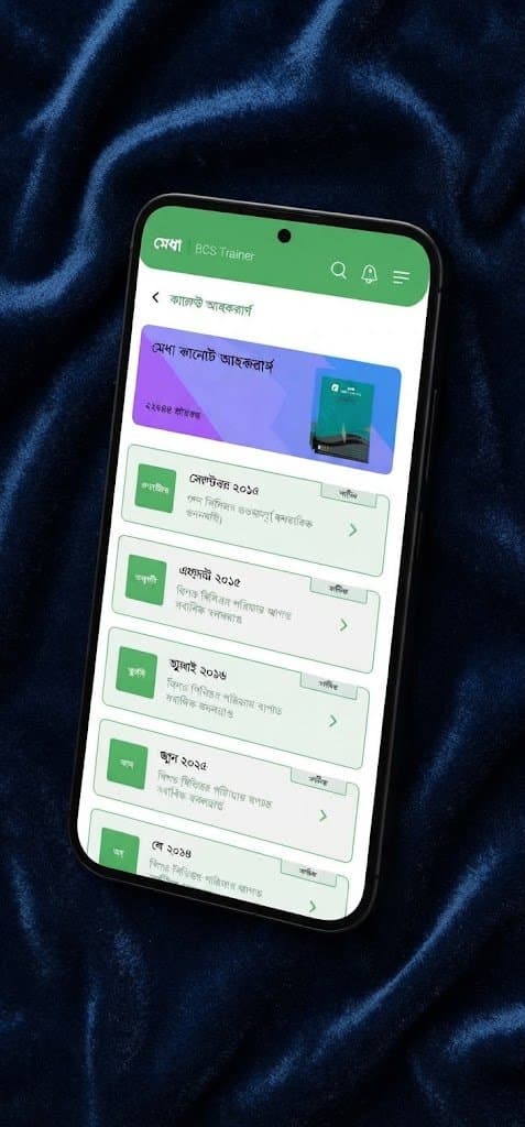 Close-up of a phone on dark blue fabric showing the Medha current affairs screen with a list of monthly editions