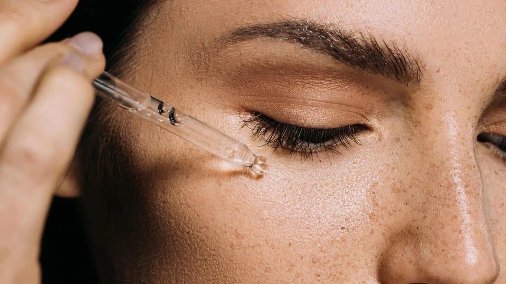 Close-up of a serum dropper held against the skin under a closed eye.