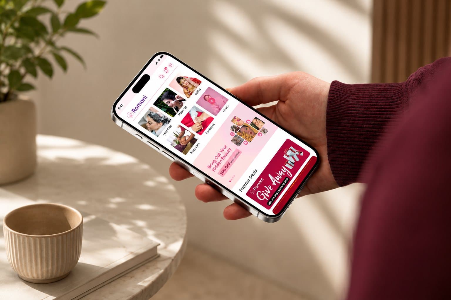 A hand holding a phone open on the Romoni app home screen, showing beauty service categories and a giveaway banner.